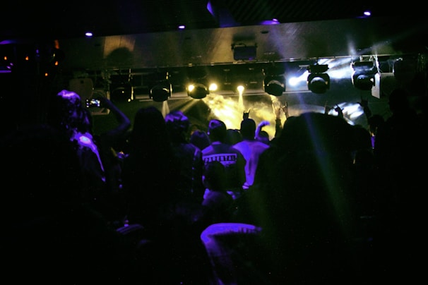 Crowd energized at a Cardian Recordz concert illuminated by neon stage lights.