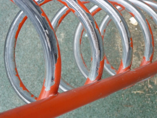 A series of weathered metal loops painted partially in red, arranged in a spiral pattern. The loops have signs of rust and are set against a textured green surface.