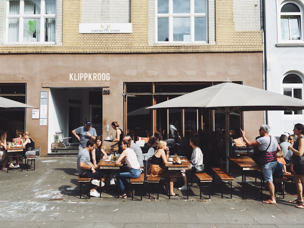 Gruppe von Menschen, die tagsüber auf Bänken mit Tischen neben der Ladenfront von Klippkroog sitzen