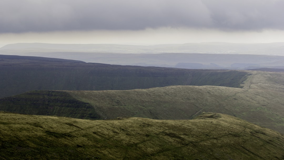 green grass covered mountain under white skies,