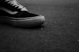 Editorial shot of a sneaker resting on a textured dark surface with subtle shadows creating depth.