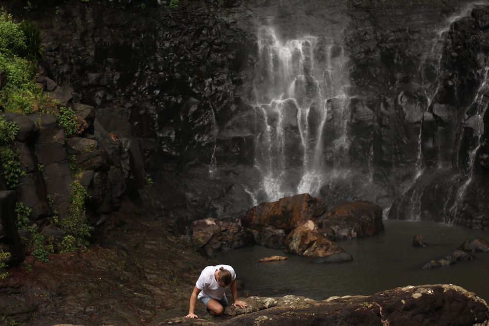 persona che si arrampica sulla roccia vicino alla cascata d'acqua