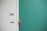 A green door with a silver door handle and a peephole. Adjacent to the door is a white wall with the number 956 and a small doorbell plate.
