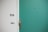 A green door with a silver door handle and a peephole. Adjacent to the door is a white wall with the number 956 and a small doorbell plate.