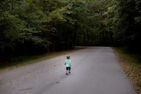 Criança pequena caminhando em estrada sem movimento com floresta ao lado