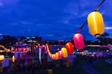 Festive outdoor event with colorful lanterns hanging from trees and guests enjoying the evening
