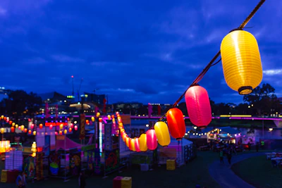 Festive outdoor event with colorful lanterns hanging from trees and guests enjoying the evening
