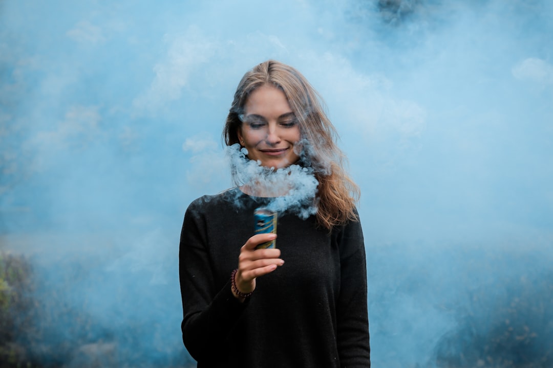 Smiling girl engulfed in the blue smoke holding smoke flare in Moscow