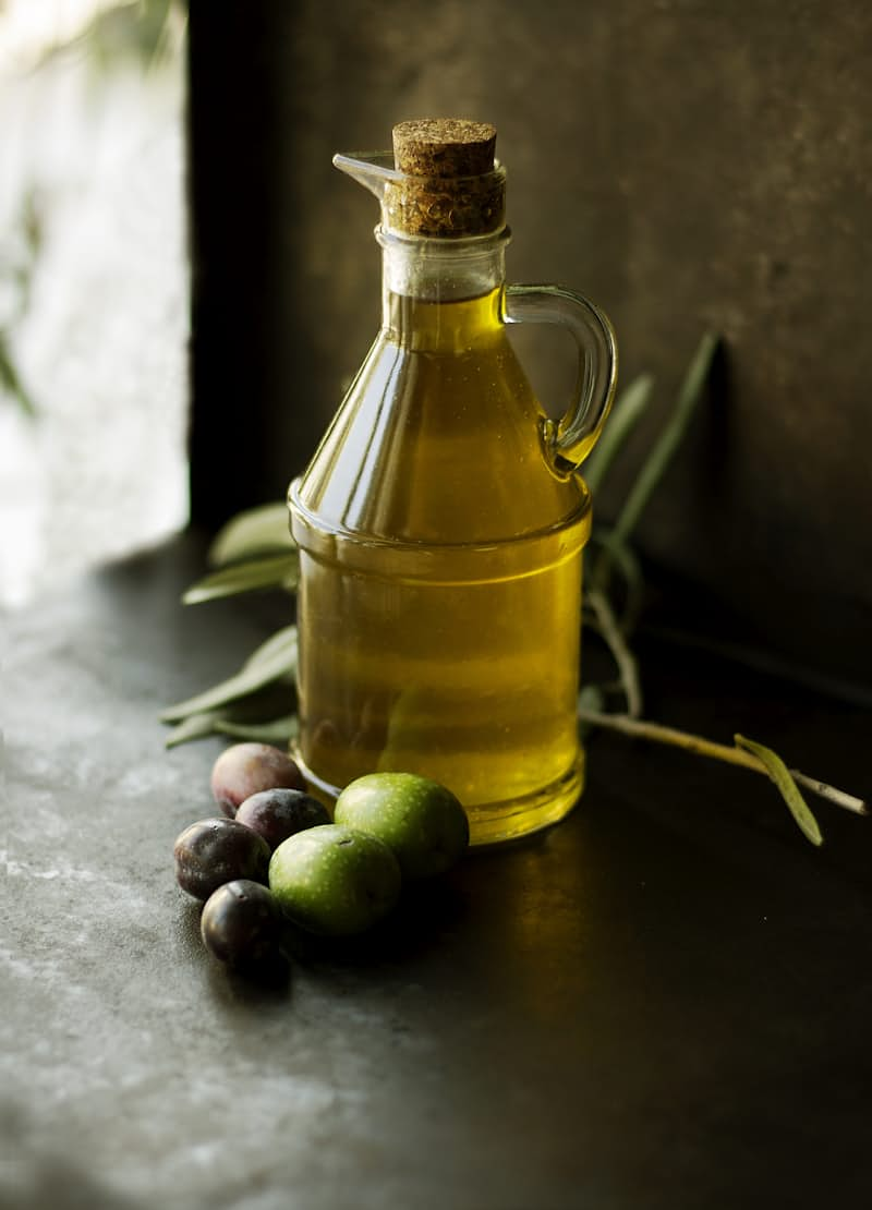 A bottle of oil surrounded by olives