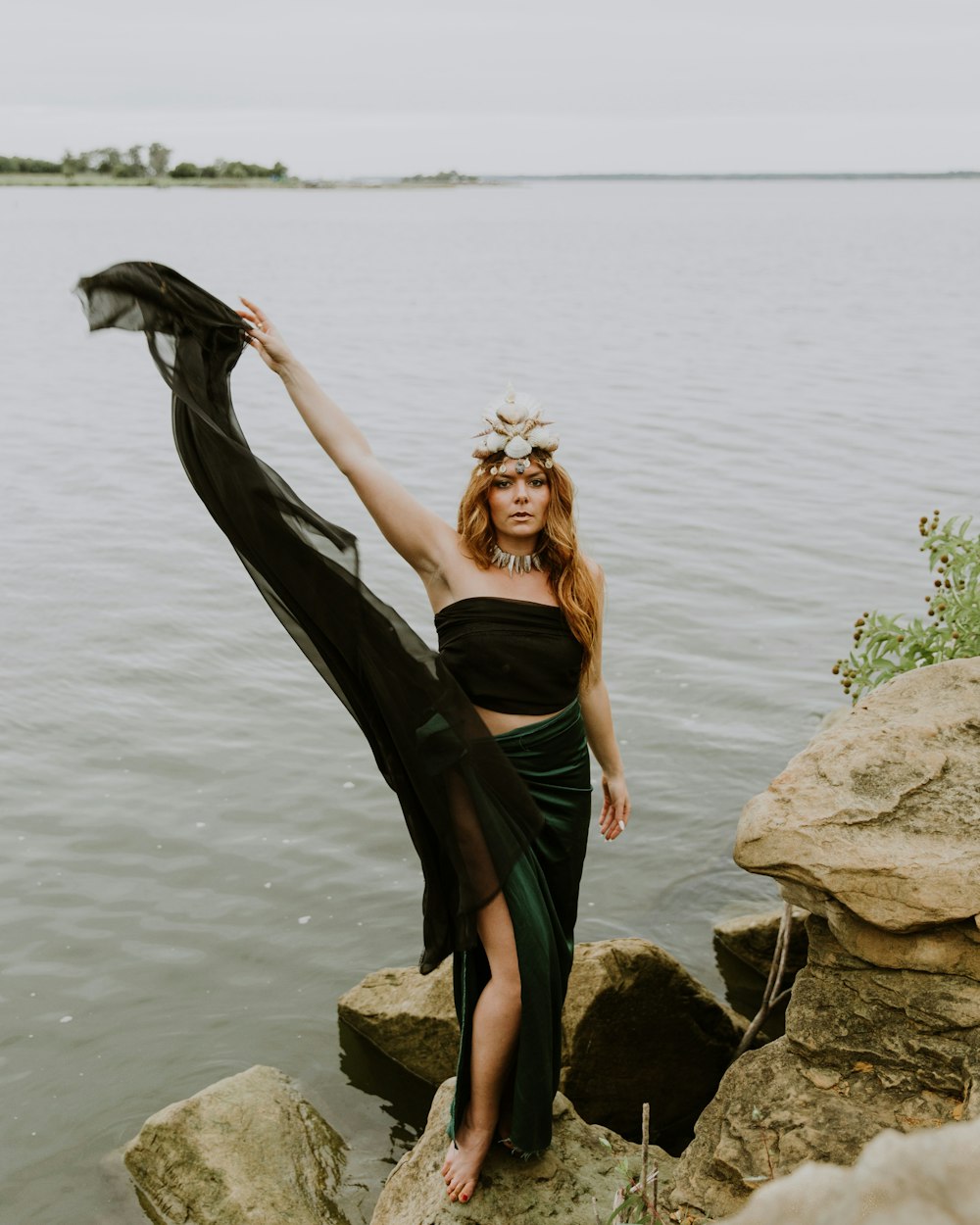 woman waving her dress on stone formation beside body of water