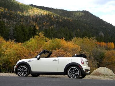 A classic convertible parked near a scenic lake with autumn trees in the background.