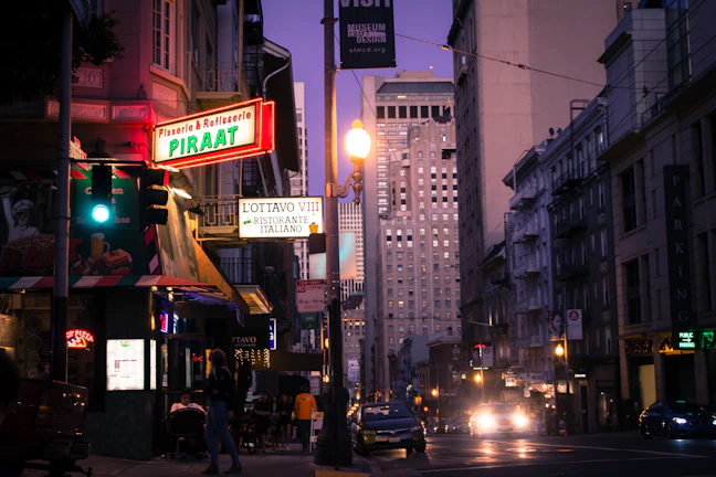 Street view of a vibrant East Orange neighborhood with restaurant signs glowing at dusk.