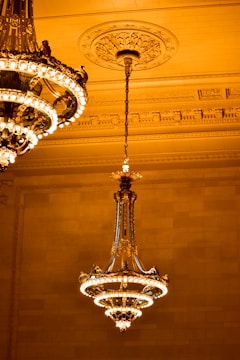 A large, ornate chandelier with multiple tiers and intricate detailing is suspended from the ceiling. The ceiling features decorative moldings and a central medallion. The warm lighting creates an elegant and luxurious ambiance.