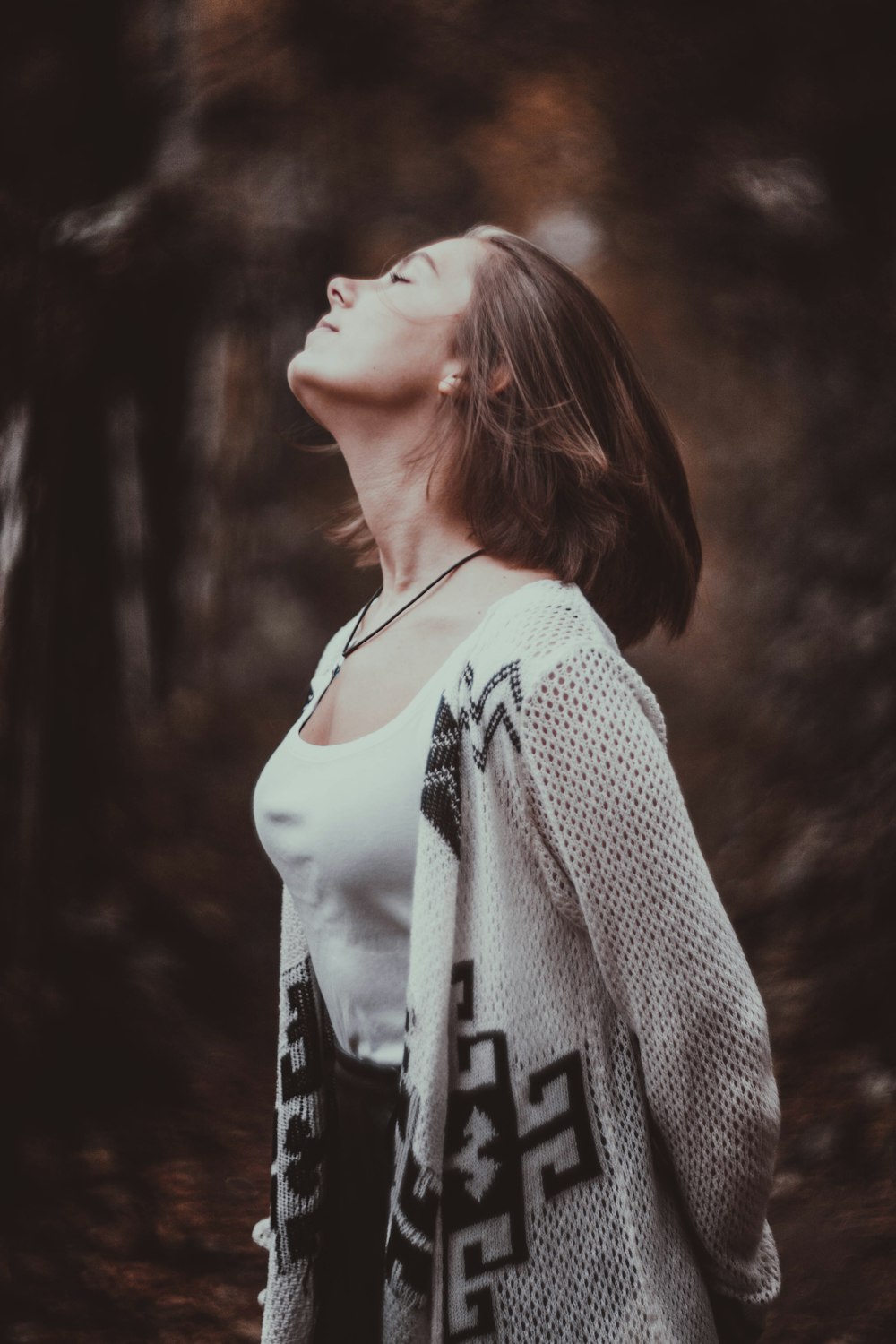 standing woman in white scoop-neck tank top with beige cardigan with her eyes close in selective focus photography