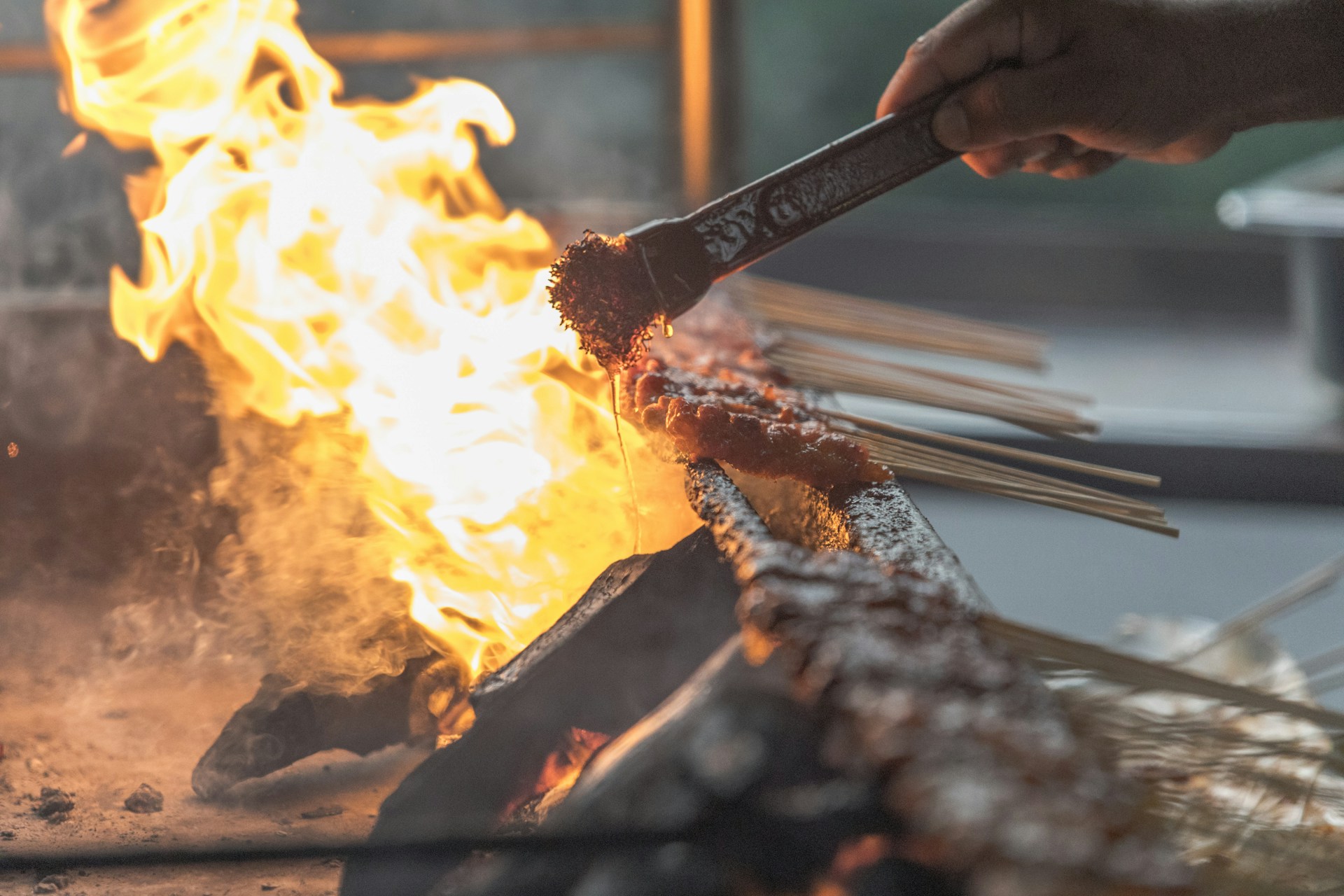 A close-up of a chef expertly flipping skewers on a barbecue grill, with flames dancing in the background.