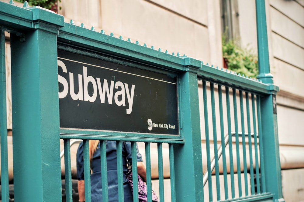 Señalización del metro en una valla metálica cian