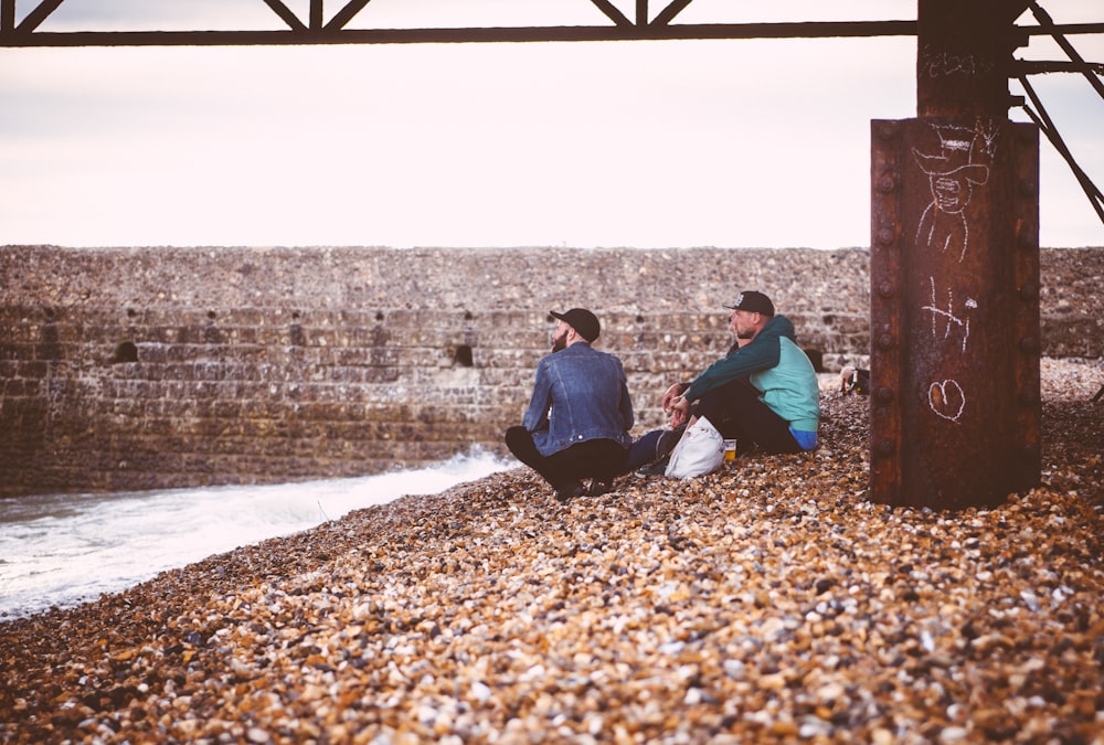 two men sitting near body of water