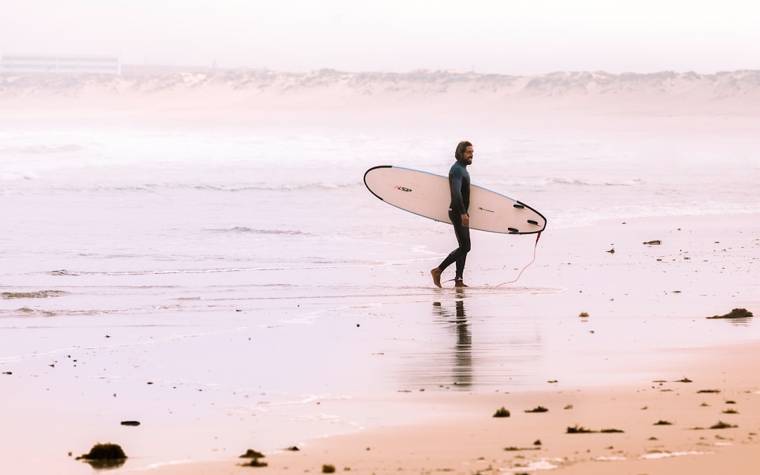 man holding surf board while standing on shore at daytime