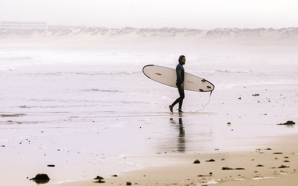 uomo che tiene la tavola da surf mentre si trova sulla riva durante il giorno