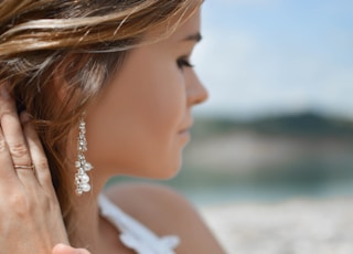 shallow focus photography of woman wearing dangling earrings holding her hair near mountain