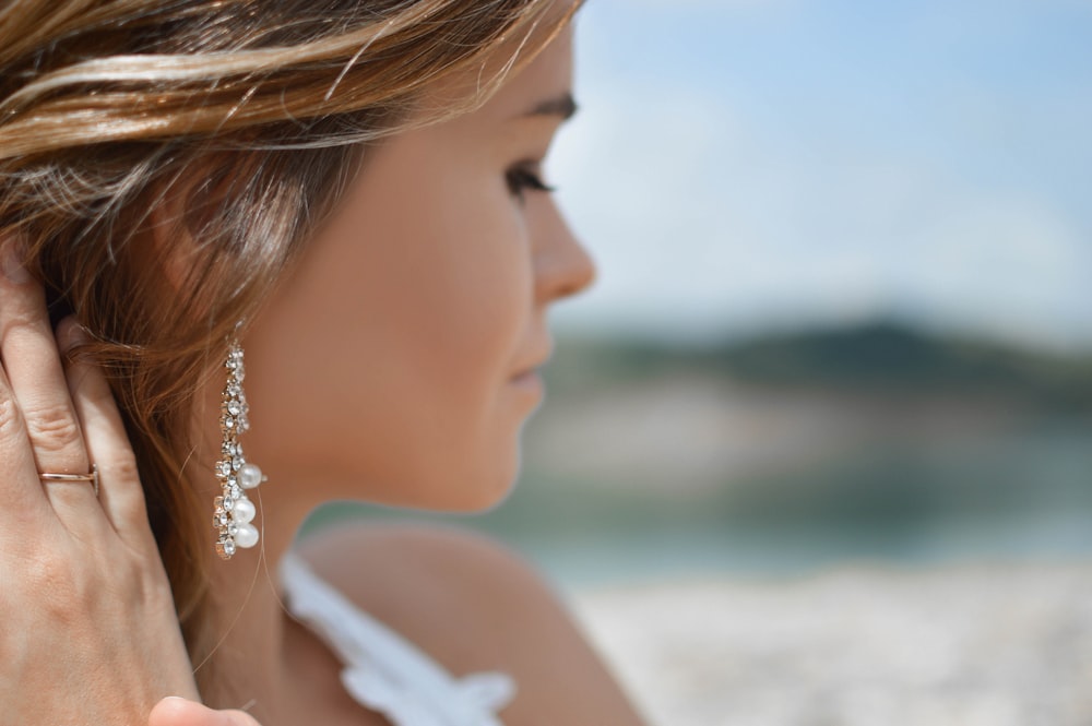 Photographie de mise au point peu profonde d’une femme portant des boucles d’oreilles pendantes tenant ses cheveux près de la montagne