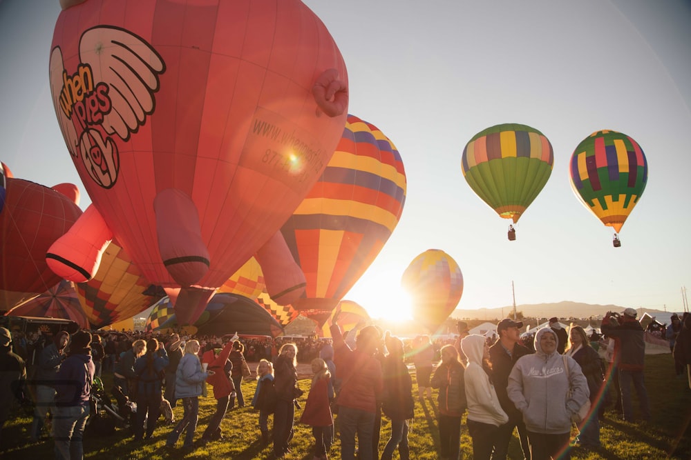 Personas cerca de globos aerostáticos de colores variados durante la puesta del sol