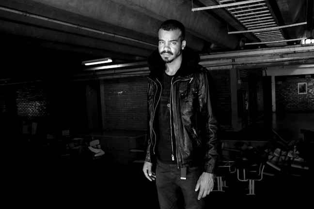 Close-up of a model wearing a sleek black leather jacket with wolf-inspired embroidery under moody lighting.