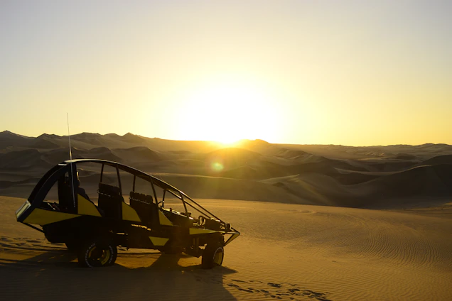 A sleek two-door buggy parked on a sandy trail with a sunset in the background.