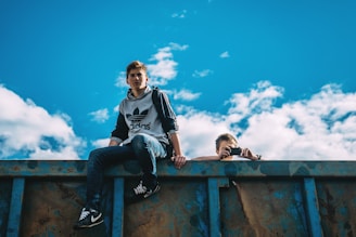 man sitting on rail beside man holding camera