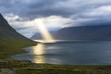 sun reflection on calm water near green mountains