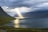 sun reflection on calm water near green mountains