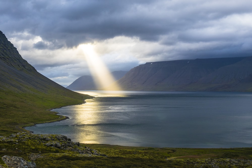 sun reflection on calm water near green mountains