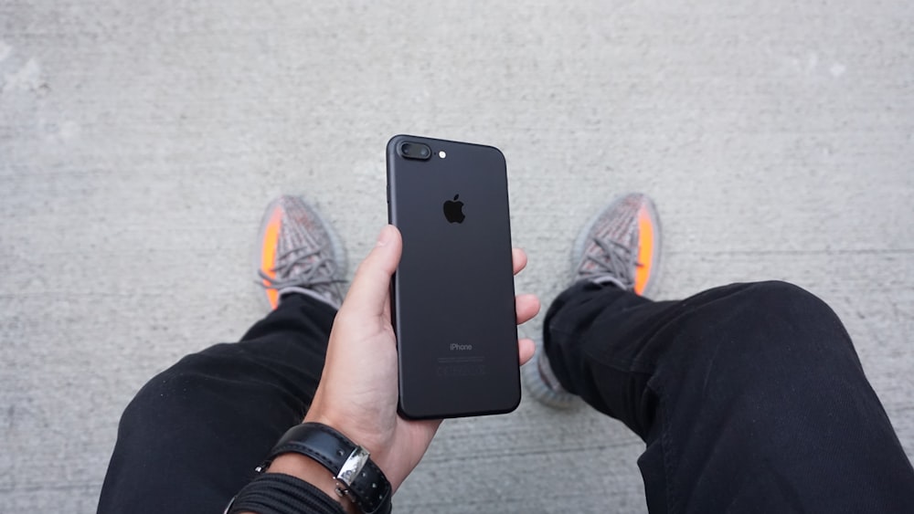 A person holding a black iPhone between their legs.