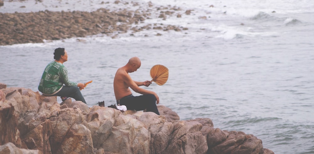 two person sitting on rock facing sea