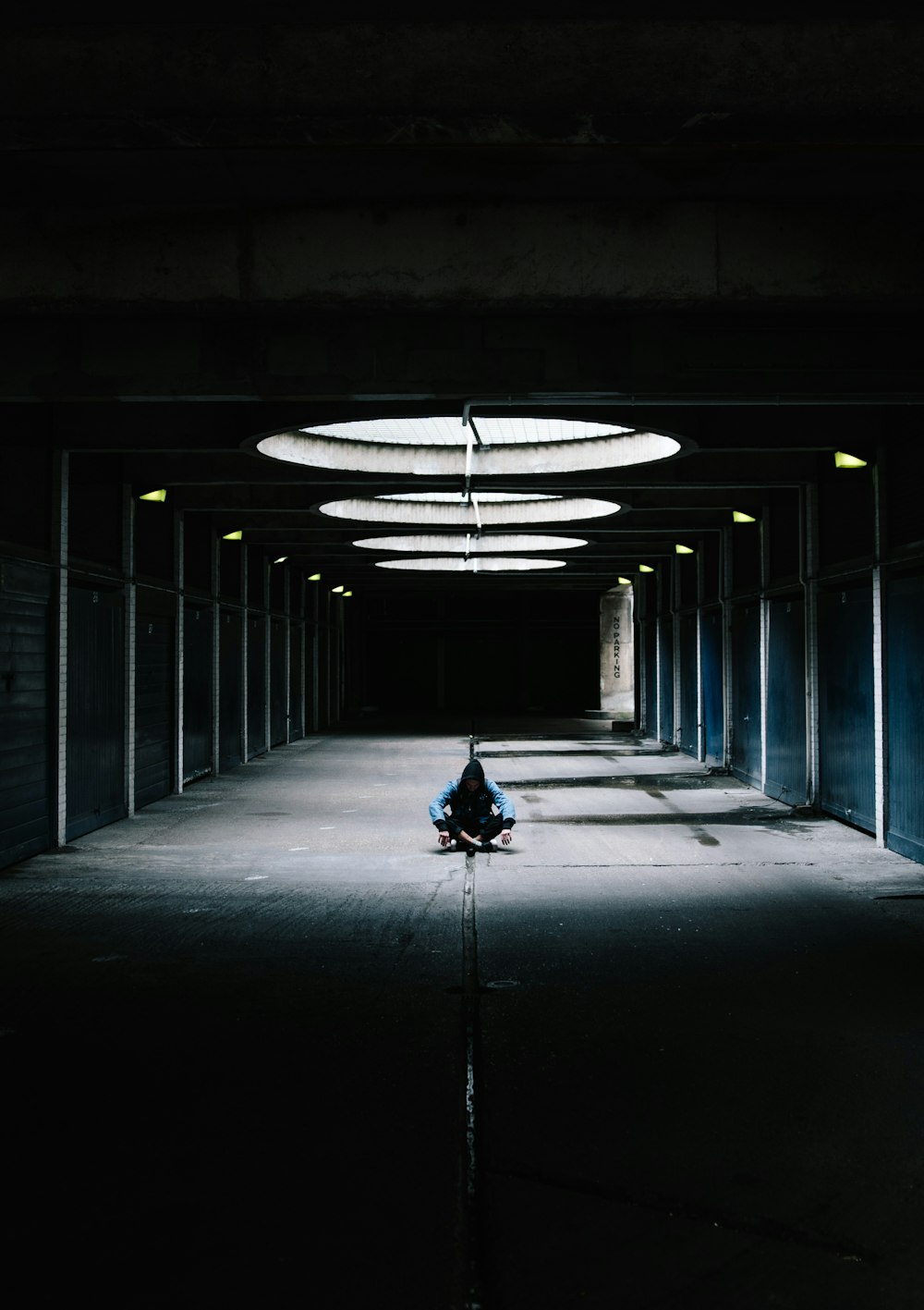 person sitting cross leg at hallway under glass ceiling between black wall