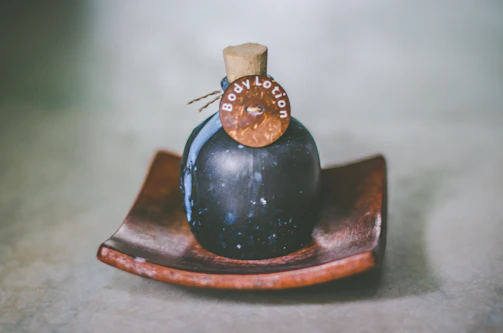 Rosaviva herbal body lotion bottle with natural herbs and pink blossoms artfully arranged on a pastel pink surface.