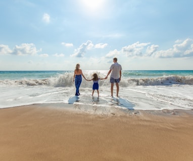 man, woman and child holding hands on seashore