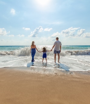 man, woman and child holding hands on seashore