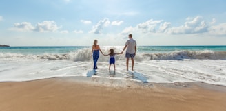 man, woman and child holding hands on seashore