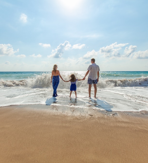 man, woman and child holding hands on seashore