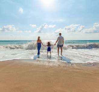 man, woman and child holding hands on seashore