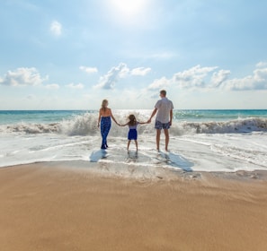 man, woman and child holding hands on seashore