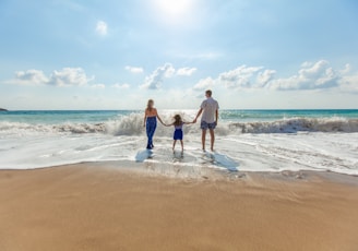 man, woman and child holding hands on seashore