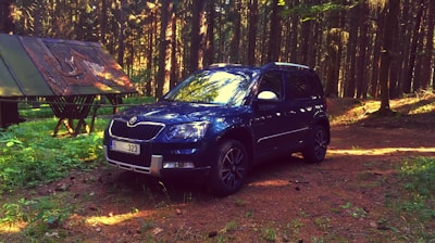 A shiny blue SUV with roof racks parked near a forest trail