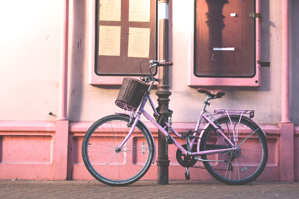 pink city bike parked on black pole in front of pink wall house