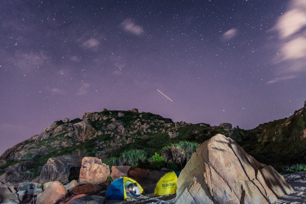 tents surrounded with green rocks under purple sky at night