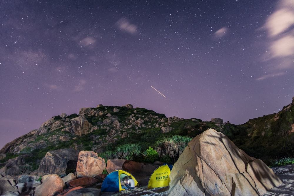 夜の紫空の下、緑の岩に囲まれたテント