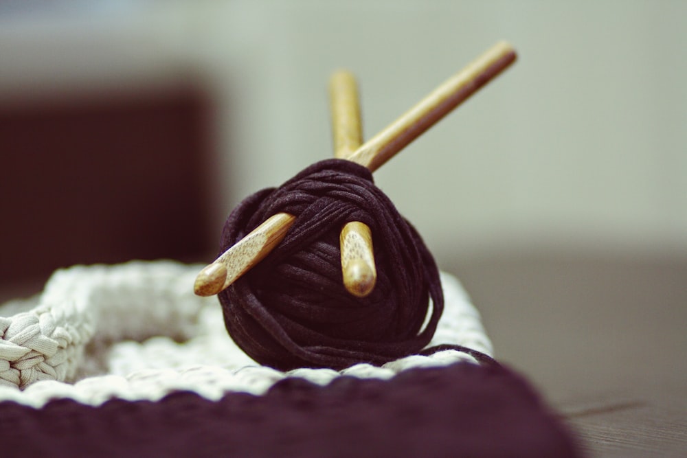白い表面の上に2つの茶色のかぎ針編みのフックが付いた茶色の糸ロール