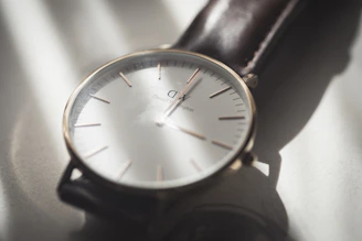 A minimalist wristwatch with a clean face and leather strap on a soft fabric background.
