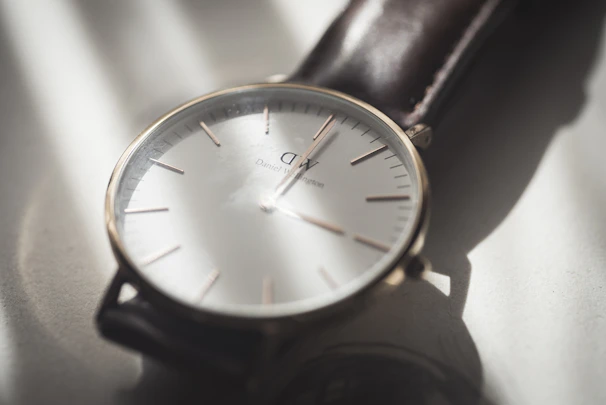 Close-up of a minimalist watch with a clean white face and leather strap on a wooden table